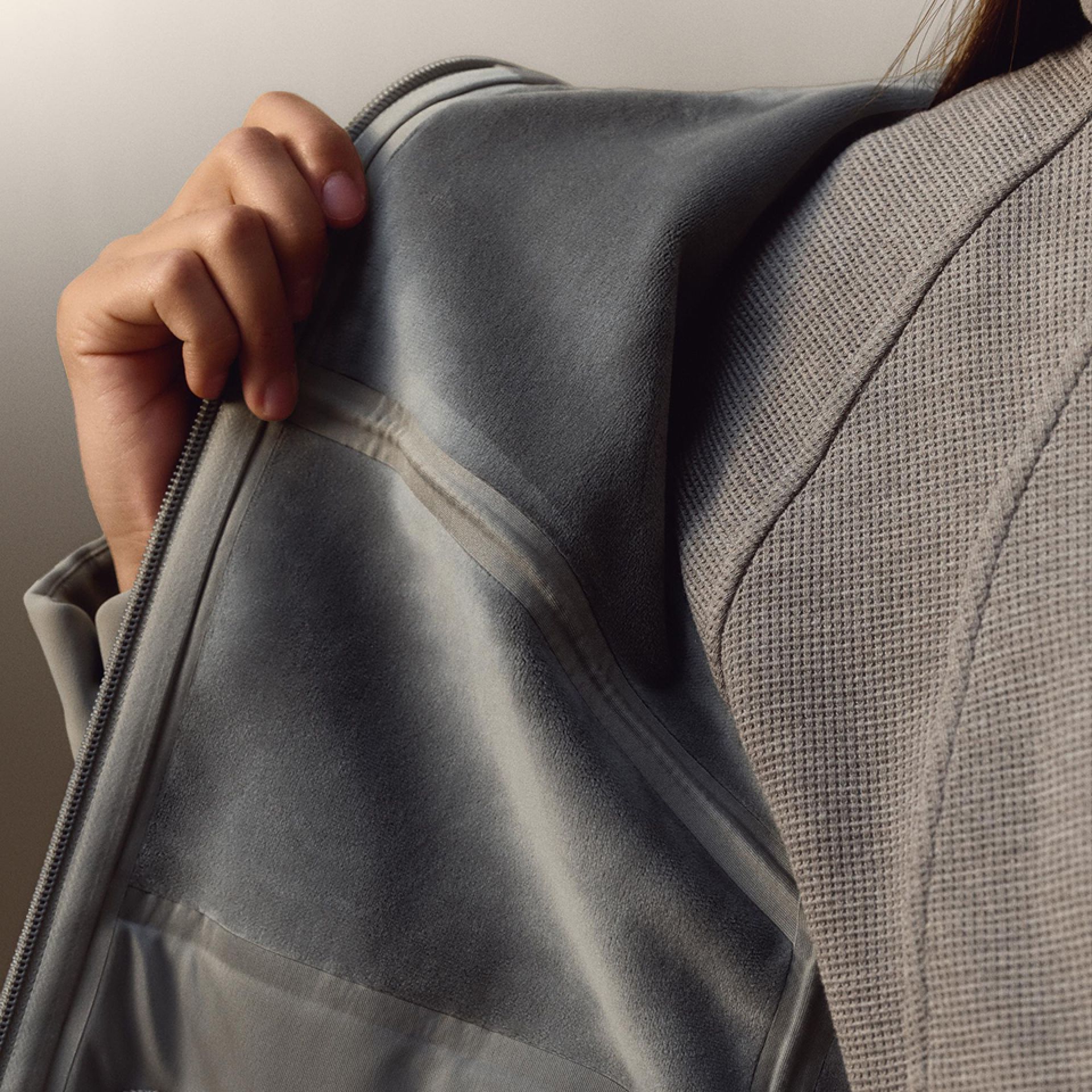 A close-up of a person wearing the Cross Chill City-to-Trail jacket with the Scuba Cropped Funnel-Neck Half Zip Waffle layered underneath while holding open one side to show the inner fabric.