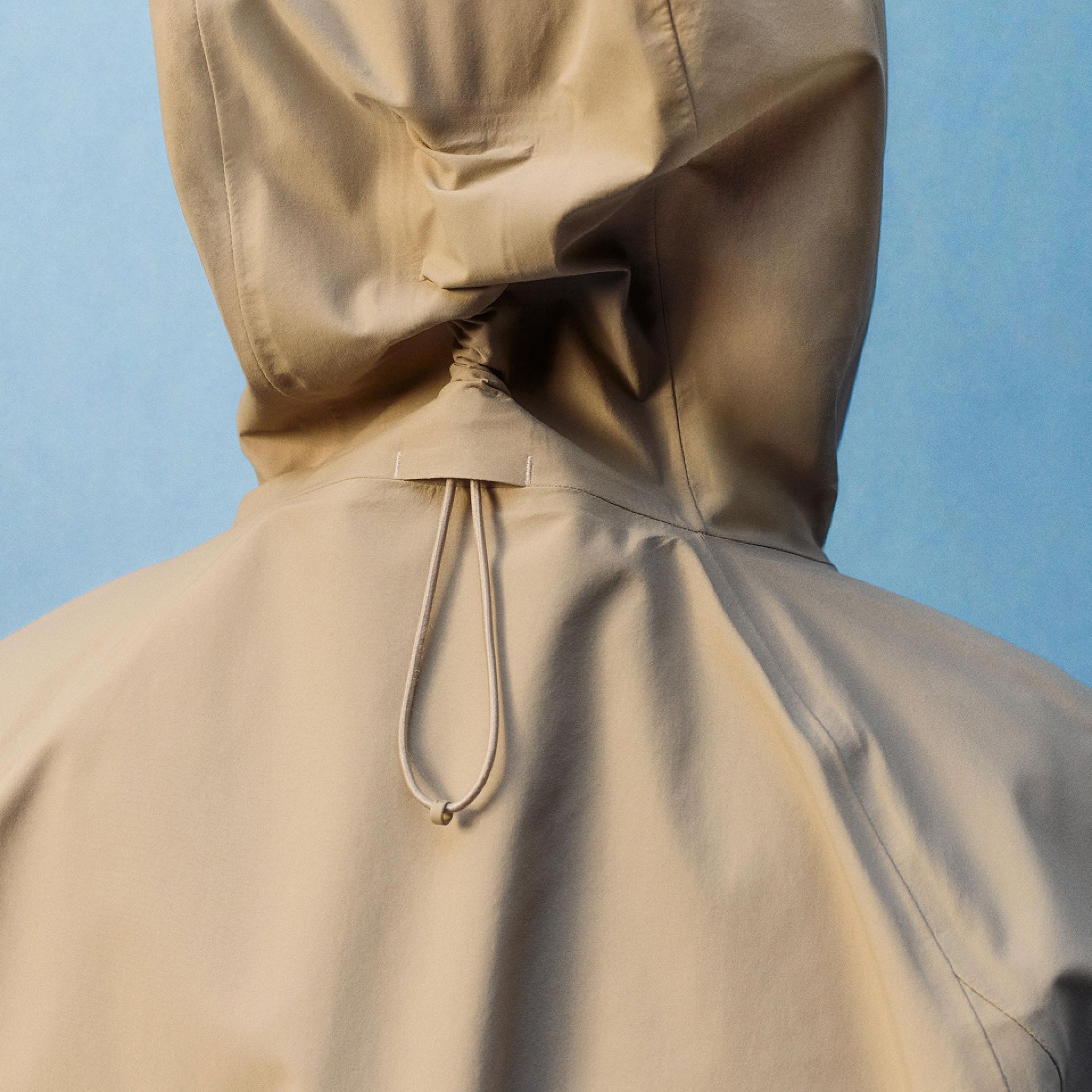 A close-up of a person wearing the Fishtail Rain Coat with a focus on the hood that features an adjustable drawcord.