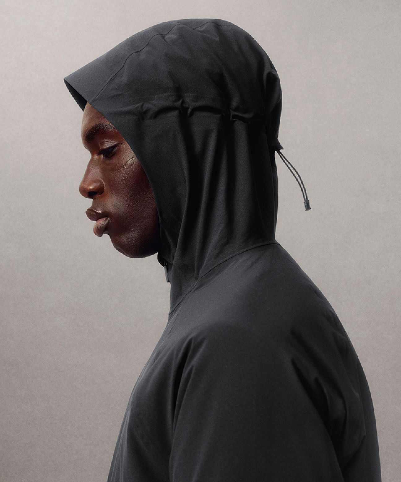 A person wearing the Stretch Glyde Waterproof Jacket with the hood up while looking down.