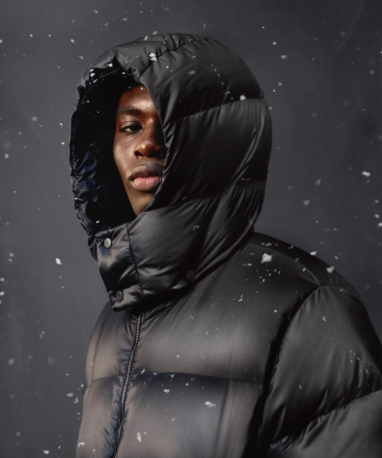 A person wearing the Always Down Puffer Jacket with the hood up while staring at the camera.