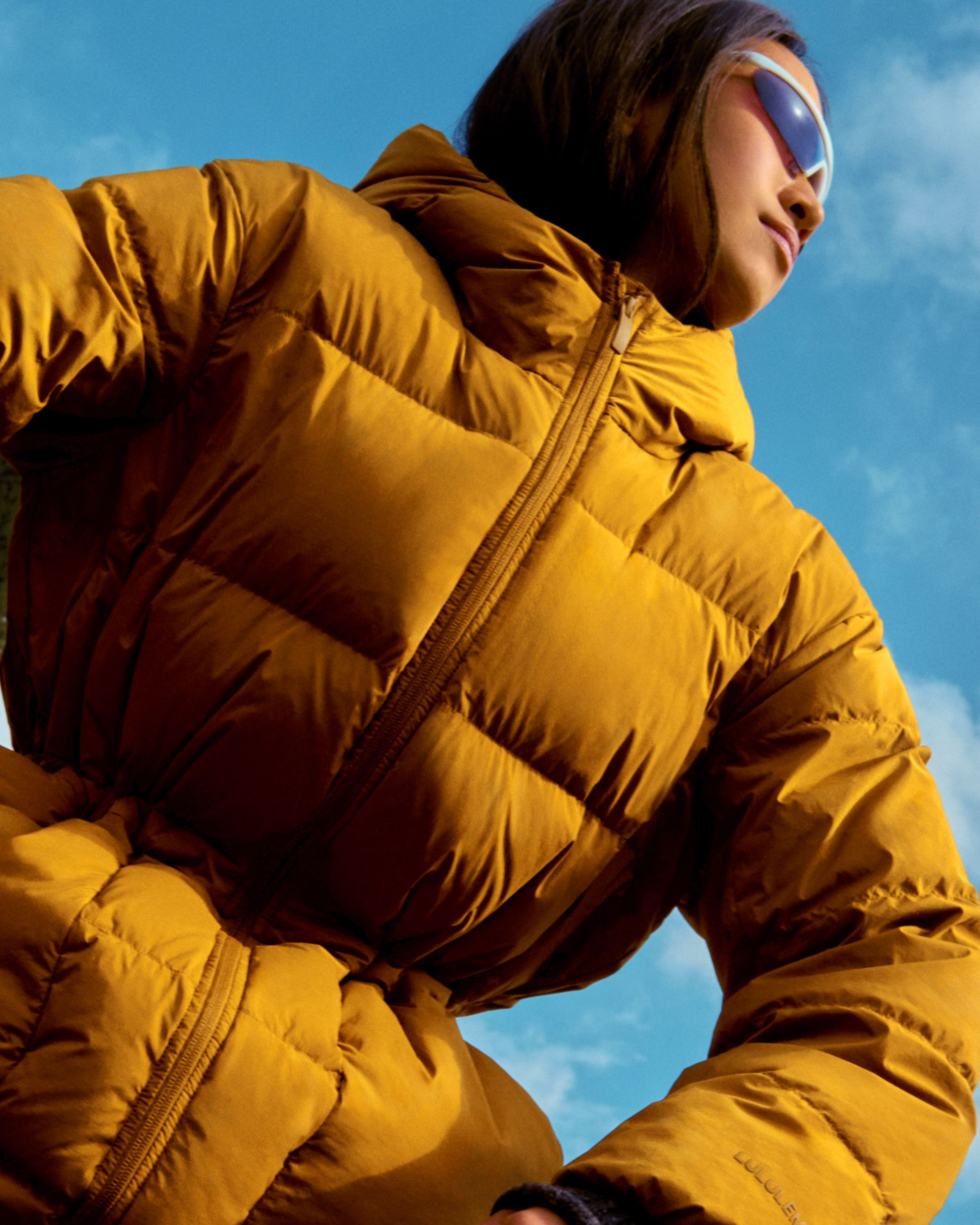 Model outdoors wearing the Insulated Cinch Puff Jacket in tan, looking up against a blue sky.