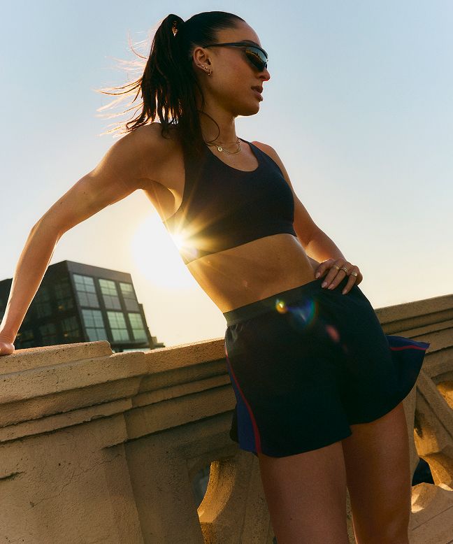 Eine Läuferin steht in lululemon Laufshorts und Sport-BH an einer steinernen Brüstung Sonnenuntergang.