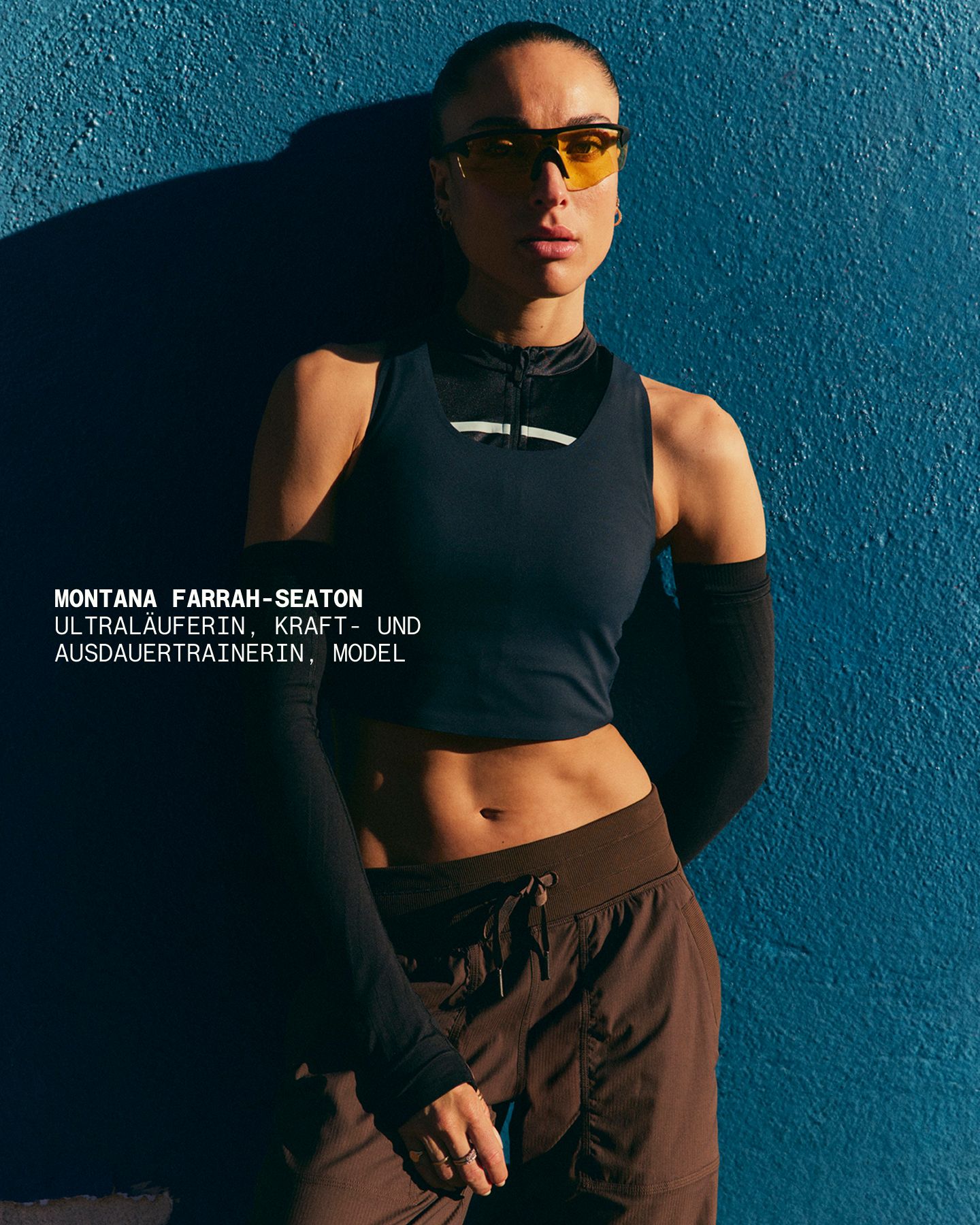 Eine Sportlerin lehnt in lululemon Laufkleidung und mit einer Performance-Sonnenbrille an einer Wand.