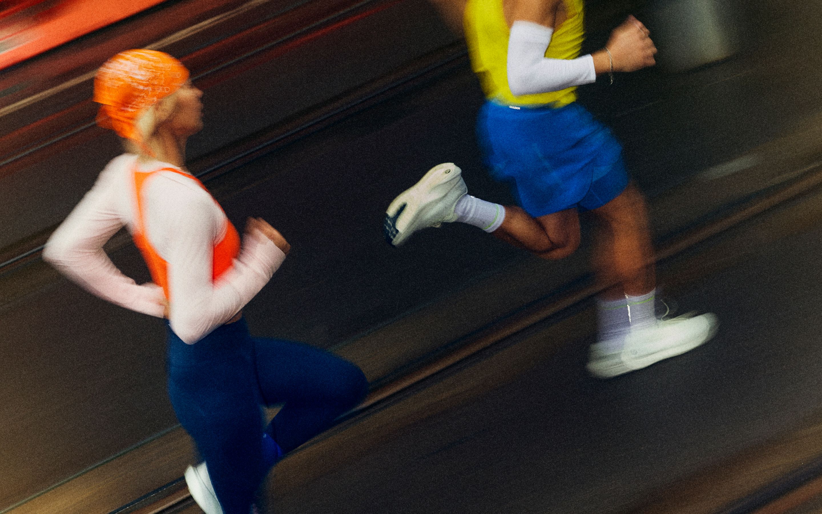 Eine Person trägt das Fast and Free-Lauftop in Orange und die Fast and Free Tights mit hohem Bund und einer Innenbeinlänge von 64 cm in einem Blauton.