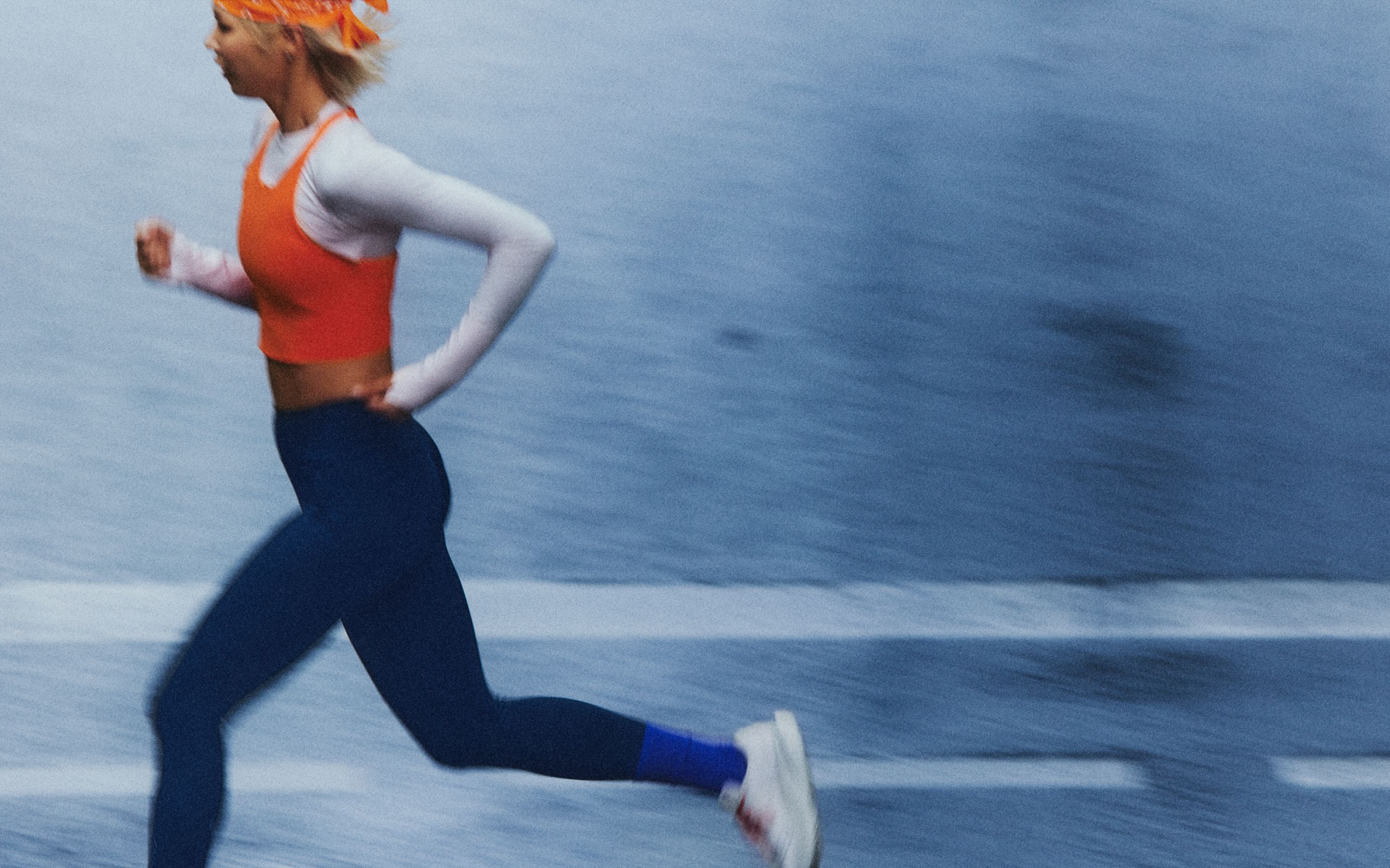 Die professionelle Athletin Haruka Koyama trägt das Fast and Free-Laufoberteil in Orange und die Fast and Free-Tights mit hohem Bund und einer Innenbeinlänge von 64 cm in Dunkelblau.
