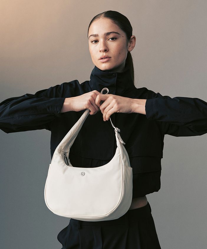 Eine Person mit der City Essentials-Schultertasche in Beige.