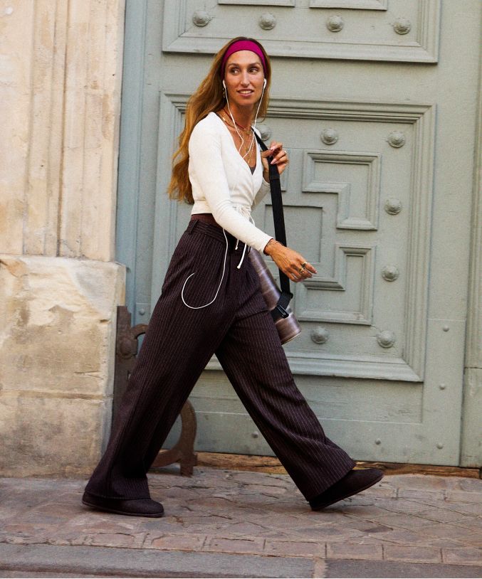 Eine Person trägt den Crop-Bolero mit langen Ärmeln in Beige und die Daydrift-Hose mit hohem Bund und weitem Bein in Schwarz. Darunter trägt sie die Align-Shorts mit einer Innenbeinlänge von 15 cm in Braun.