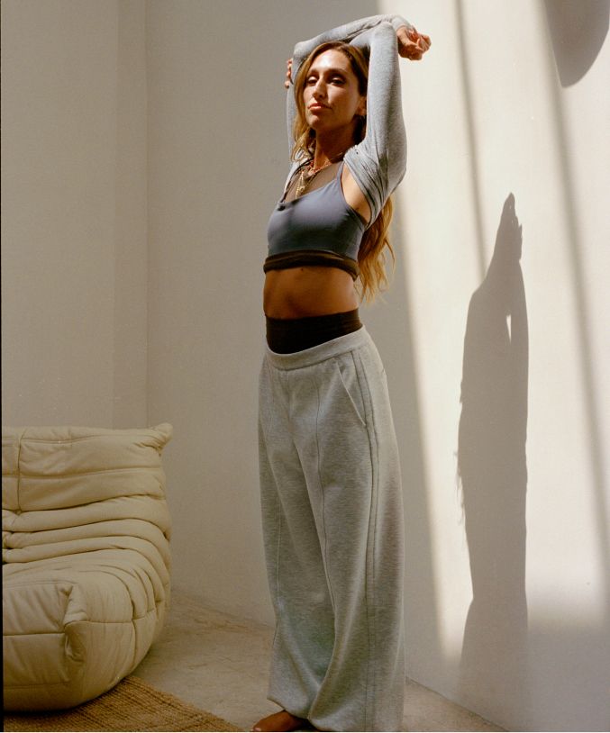 Eine Person trägt die Smooth Spacer-Hose mit hohem Bund und weitem Bein in Grau, das Align-Top mit Racerback in Taillenlänge in Braun und das Swiftly Tech-Langarmshirt sowie den Flow Y-BH in einem Blaugrauton.