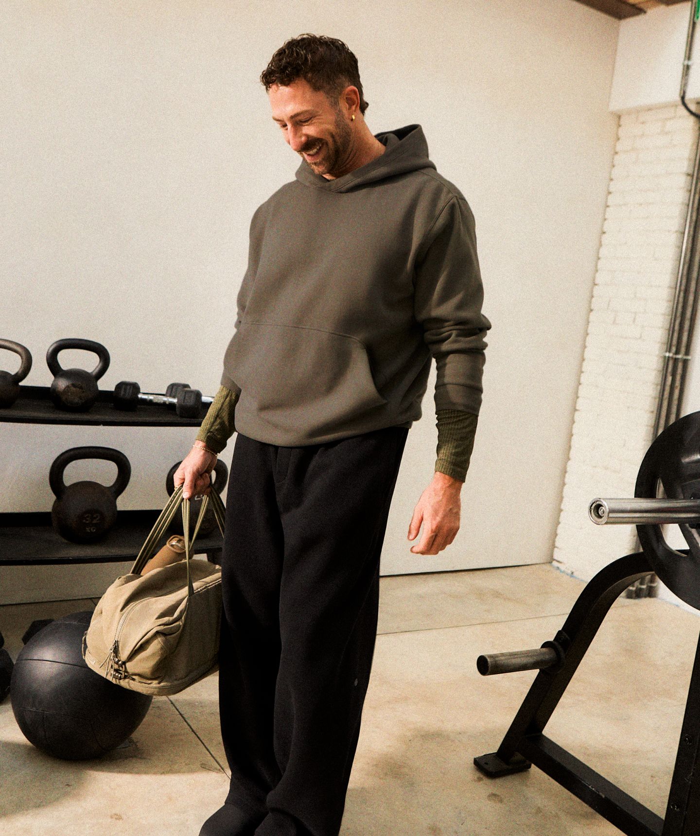 Eine Person trägt den Steady State-Hoodie aus SuperLoft® in einem Grünton über einem Metal Vent Tech-Langarmshirt in einem Grünton, dazu die Steady State-Hose aus SuperLoft® in Schwarz.