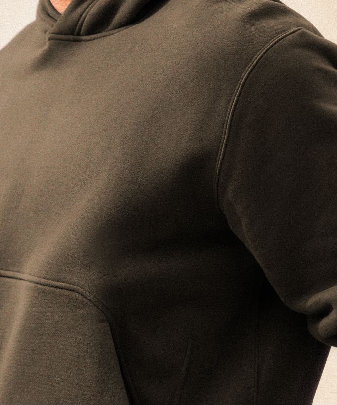 Eine Person trägt den Steady State-Hoodie aus SuperLoft® in einem Grünton über einem Metal Vent Tech-Langarmshirt in einem Grünton, dazu die Steady State-Hose aus SuperLoft® in Schwarz.