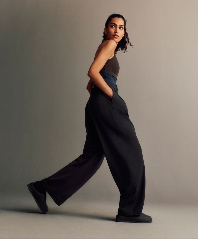 Eine Person trägt den Crop-Bolero mit langen Ärmeln in Beige und die Daydrift-Hose mit hohem Bund und weitem Bein in Schwarz. Darunter trägt sie die Align-Shorts mit einer Innenbeinlänge von 15 cm in Braun.