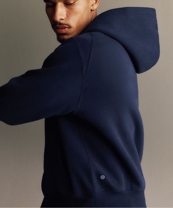 Eine Person trägt den Steady State-Hoodie aus SuperLoft® in einem Grünton über einem Metal Vent Tech-Langarmshirt in einem Grünton, dazu die Steady State-Hose aus SuperLoft® in Schwarz.