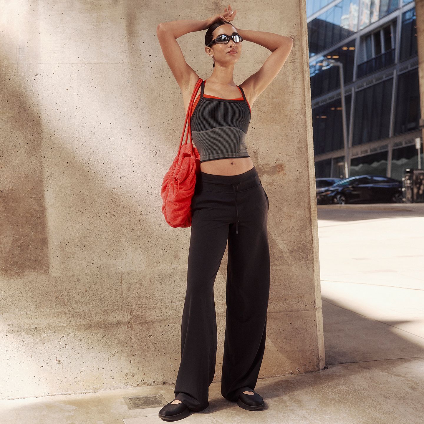 Eine Person trägt das Salutations-Yoga-Tanktop in Schwarz/Grau und die Groove-Hose mit hohem Bund und weitem Bein in Schwarz.