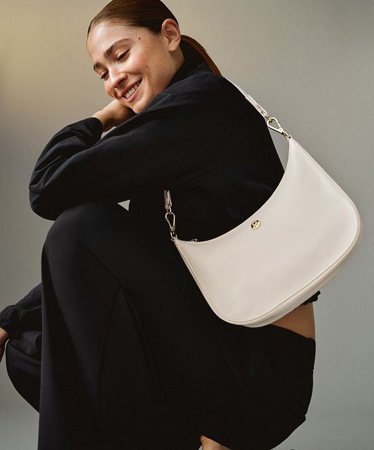 A person sits on the floor wearing the City Essentials Bag on their shoulder.