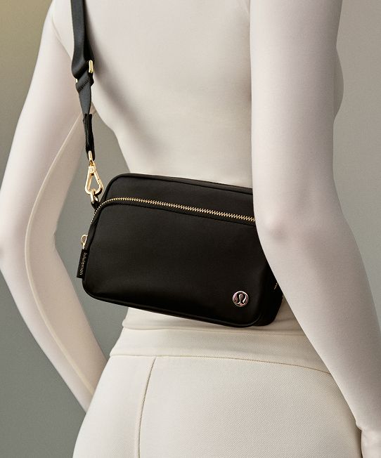 A person sits on the floor wearing the City Essentials Bag on their shoulder.