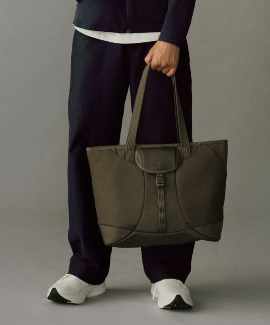A close-up of a person holding the Daily Dispatch Tote Bag in their left hand.