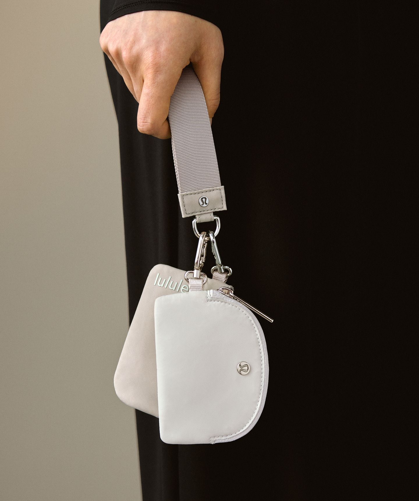 A close-up shot of a person's hand holding the strap of the Dual Pouch Wristlet.