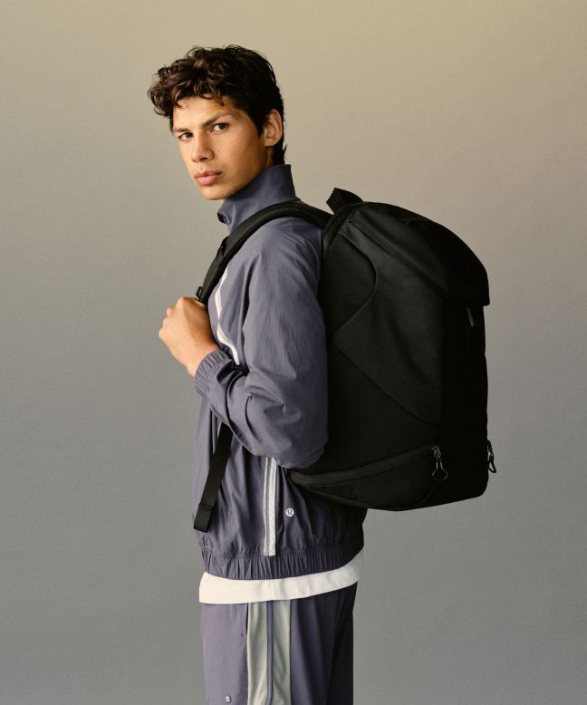 A person stands and looks to their left with a backpack on their back.