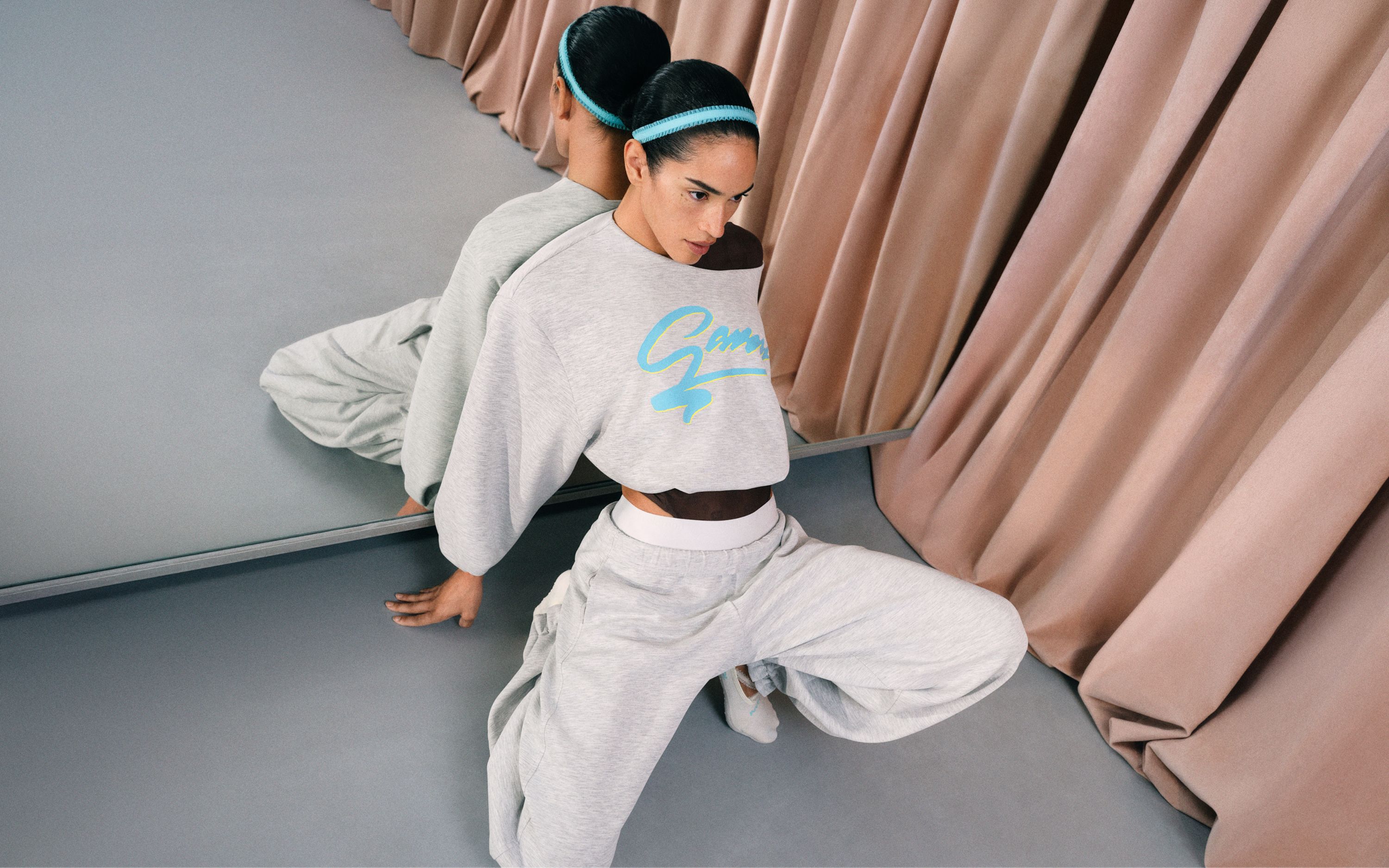 A person leaning on a mirror posing while wearing a matching set featuring an oversize sweatshirt and pants from the collection