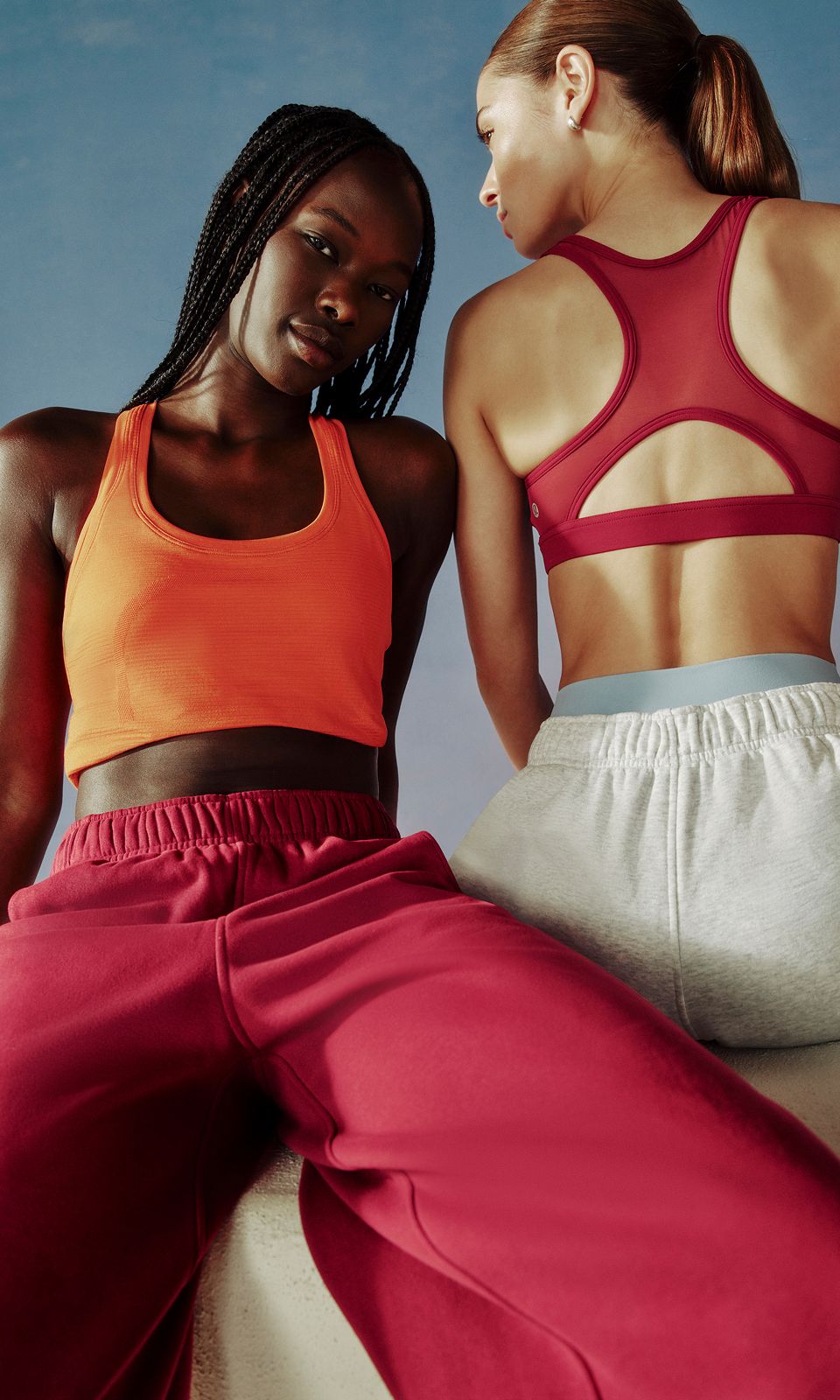 An image of two people sitting on a ledge. One is facing forward and wearing the new Scuba Evolve Straight Leg Pant, while the other has their back turned and wearing the new Scuba Evolve Oversized Short.