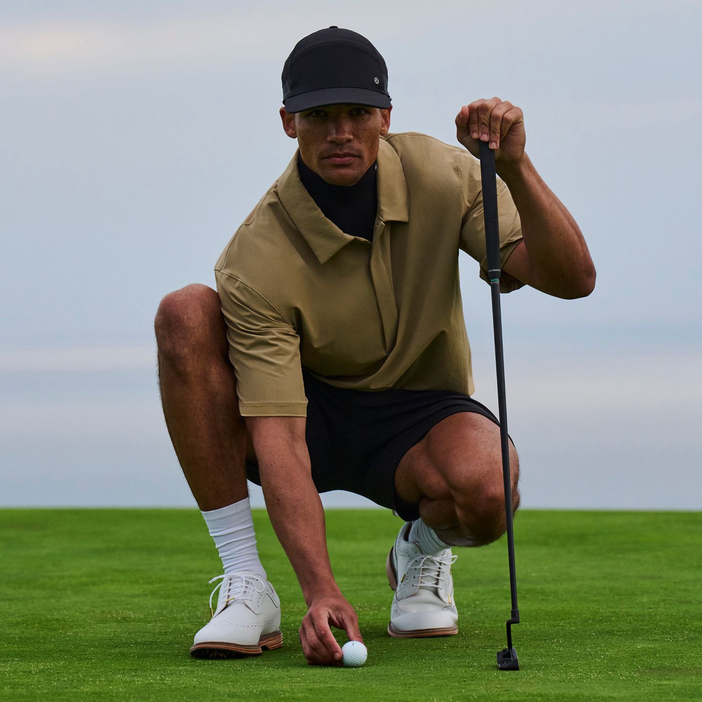 Un golfeur s’accroupit pour analyser son coup roulé. Il porte le pullover de golf hydrofuge.