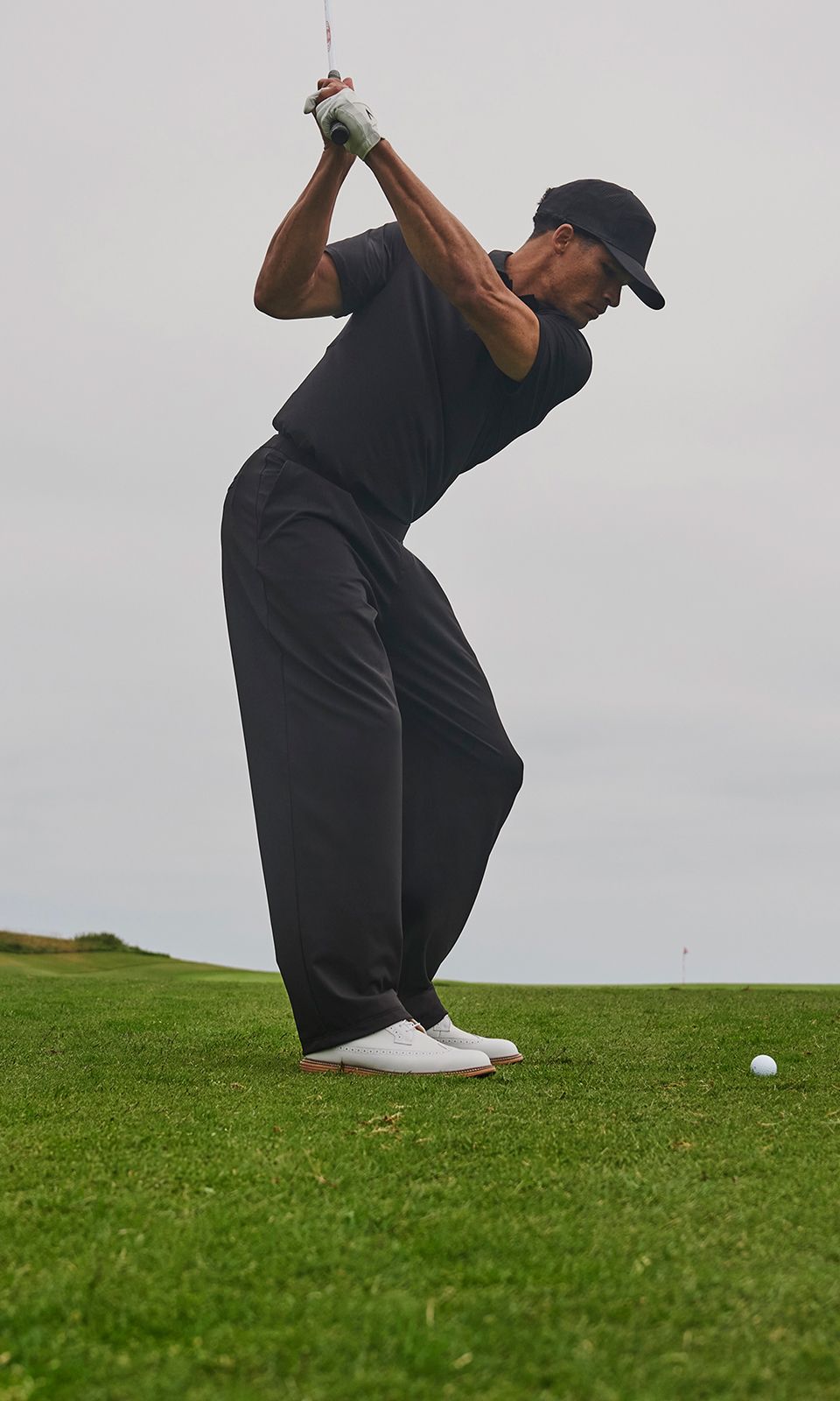 A golfer wears the Daydrift Trouser. They prepare to swing. They tend the flag. They crouch down to read the green. They look ahead after striking the ball.