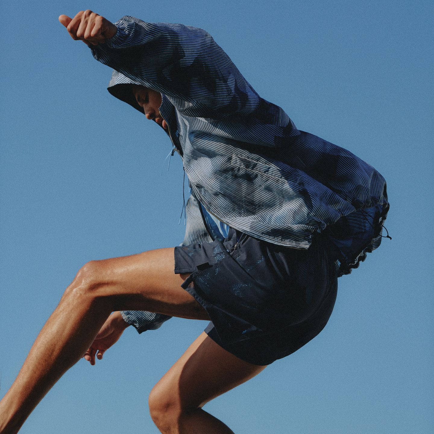 A person in motion jumps in the air with their arms and legs outstretched. They are wearing clothes from the summer 2026 SLNSH collection.