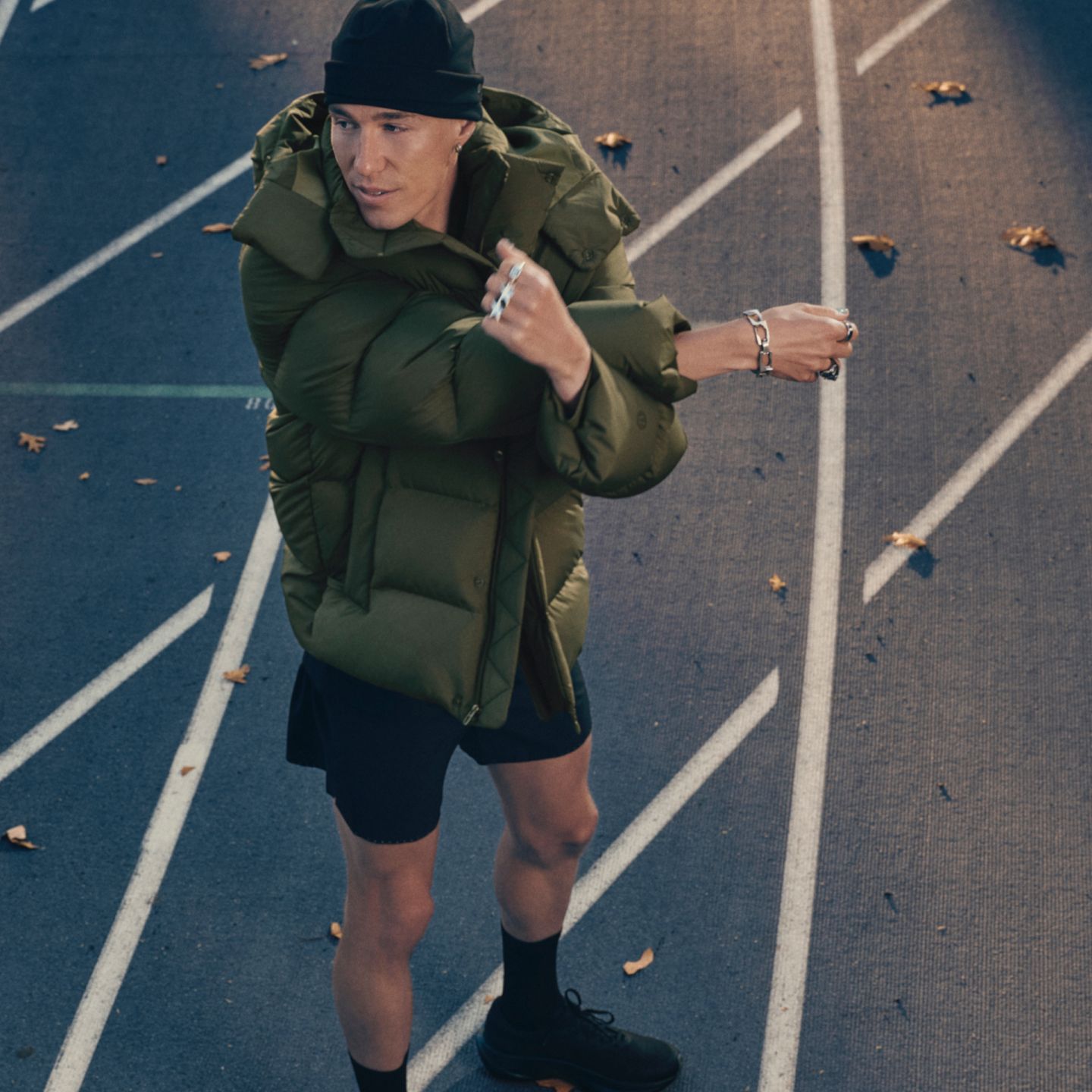 A person wearing shorts, a beanie, and a Wunder Puff jacket stretching outside.