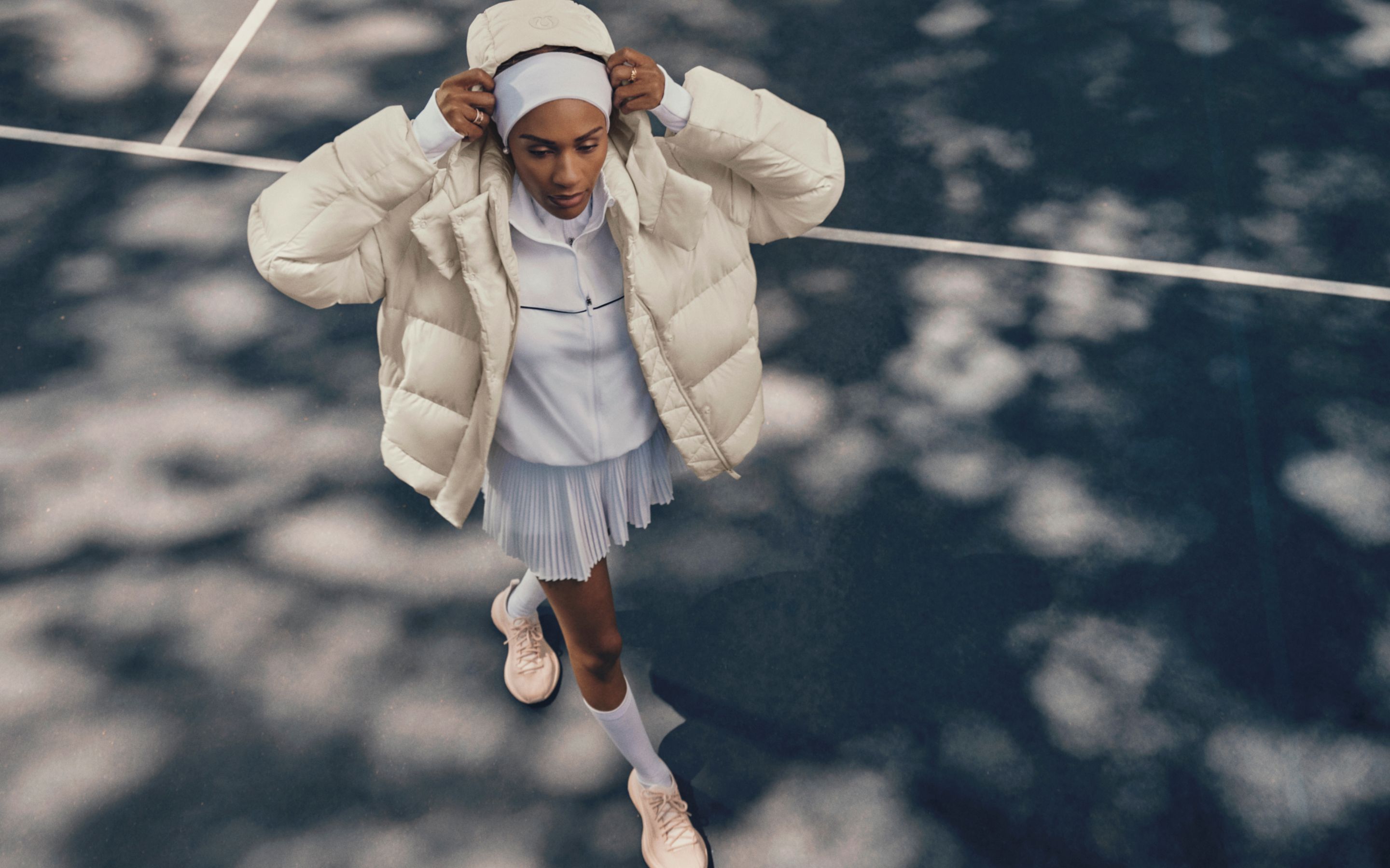 A person standing on a tennis court wearing a Wunder Puff jacket and putting the hood on over their head. 