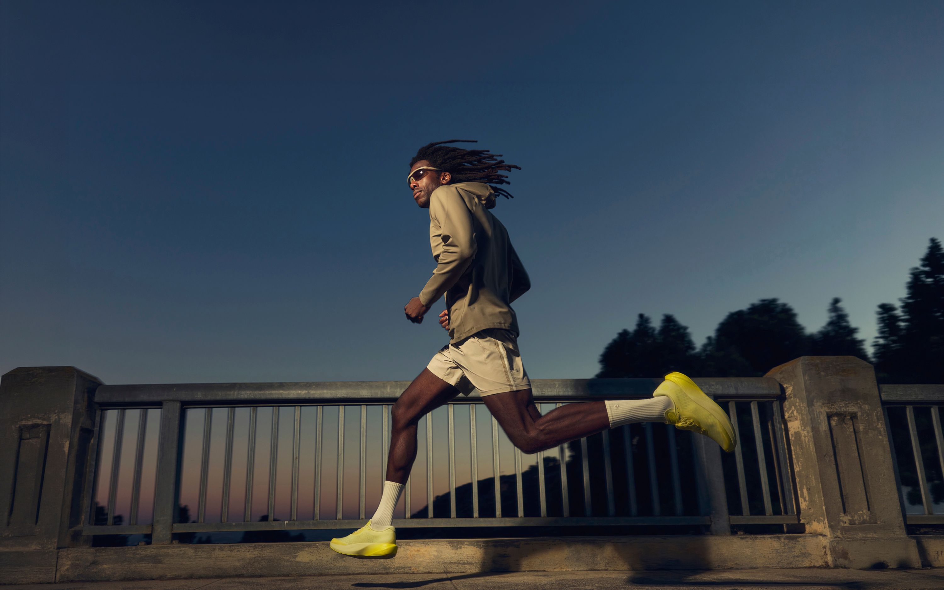 A person running outside at dusk in the Pace Breaker Short 7” *Glyde, Rulu Fleece Hoodie and Split Shift Running Shoes.