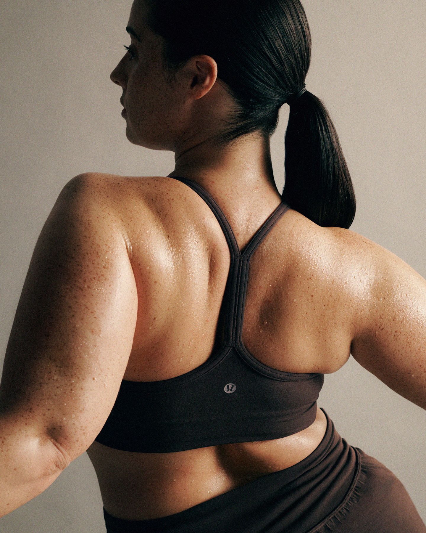 A person with outstretched arms leans back against a bar, wearing the racerback Flow Y Bra.