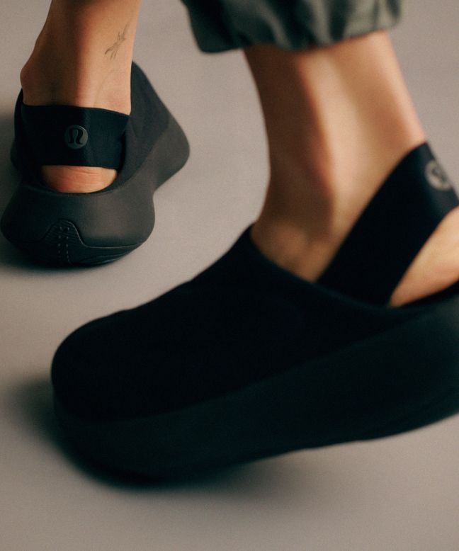 A person walks away wearing black ZenMode mules with the elastic strap worn at their heel.