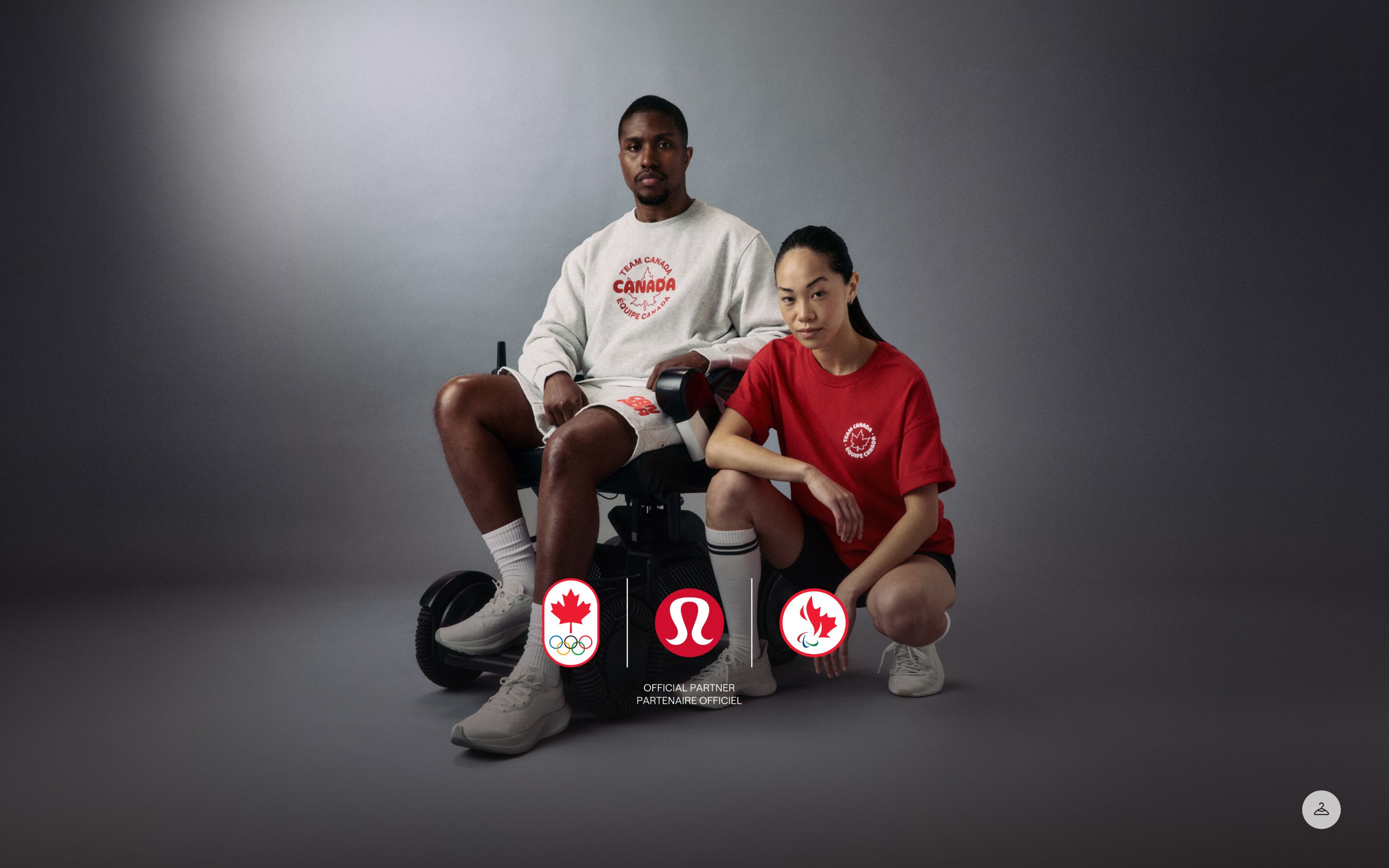 A para-athlete in a wheelchair is wearing the Team Canada Steady State Crew and Steady State Classic-Fit Short. Standing beside them is an athlete wearing the Team Canada Cotton Jersey Short Sleeve T-shirt. 
