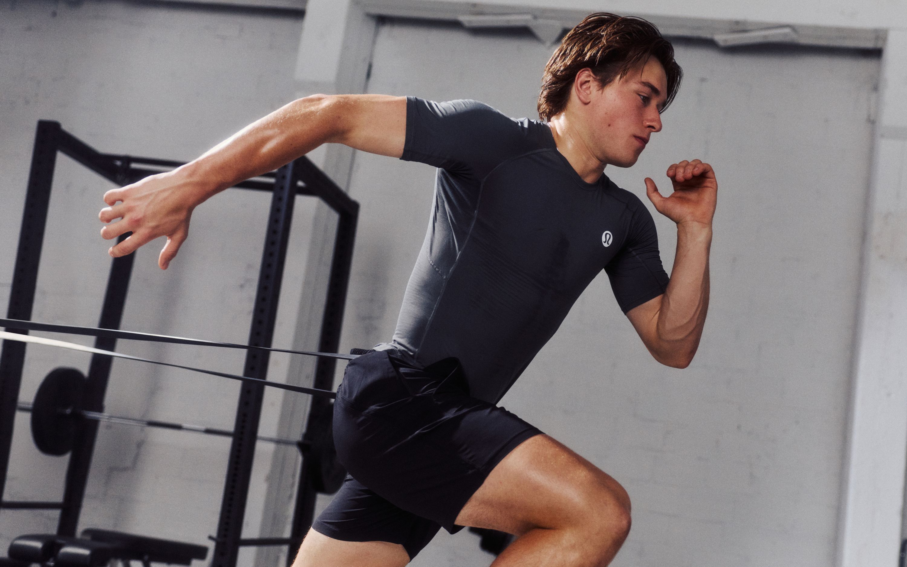 Professional Ice Hockey Player and lululemon Ambassador Macklin Celebrini drives forward against a resistance band while wearing the Unrestricted Power Shirt.  