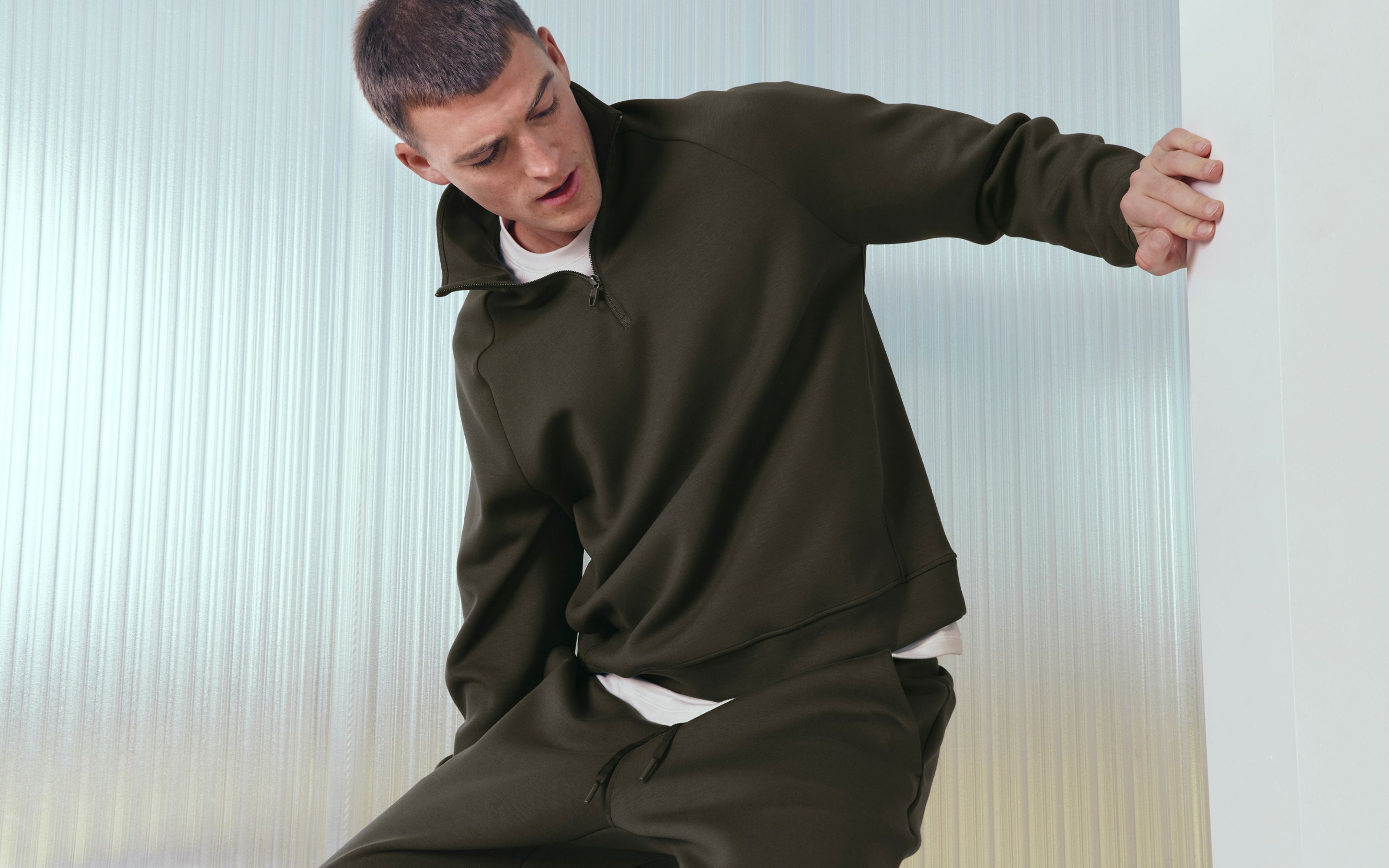 A person leans on a wall while wearing the Smooth Spacer Quarter Zip.