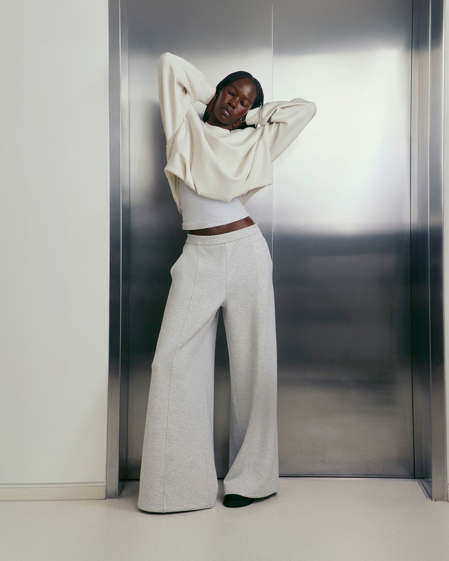 A person stands, stretching, in front of an elevator in the Smooth Spacer Oversized Crew.