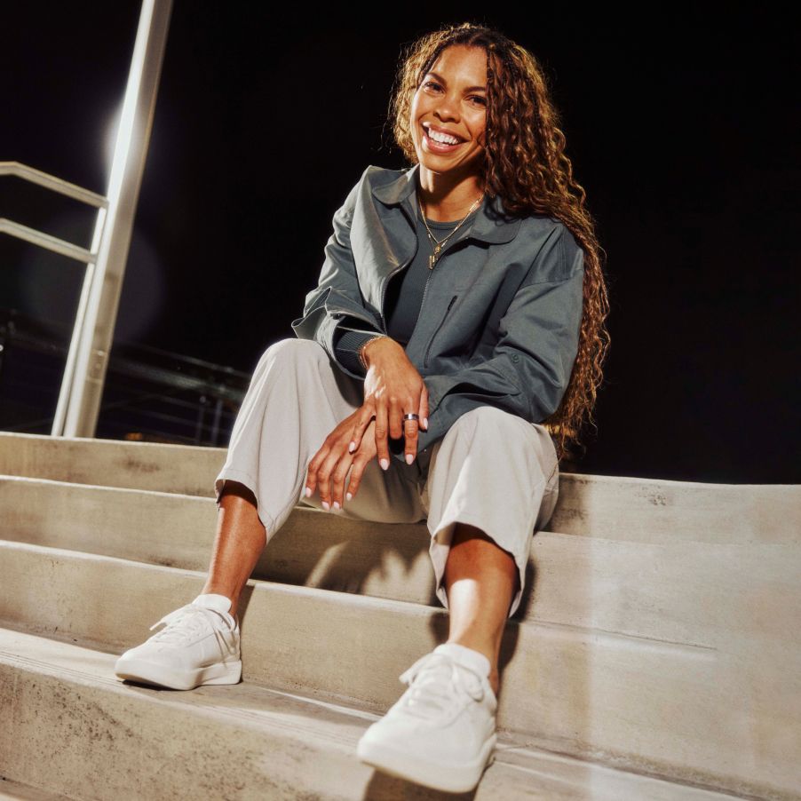 Woman sitting on steps smiling at the camera, wearing the new Cityverse Sneaker