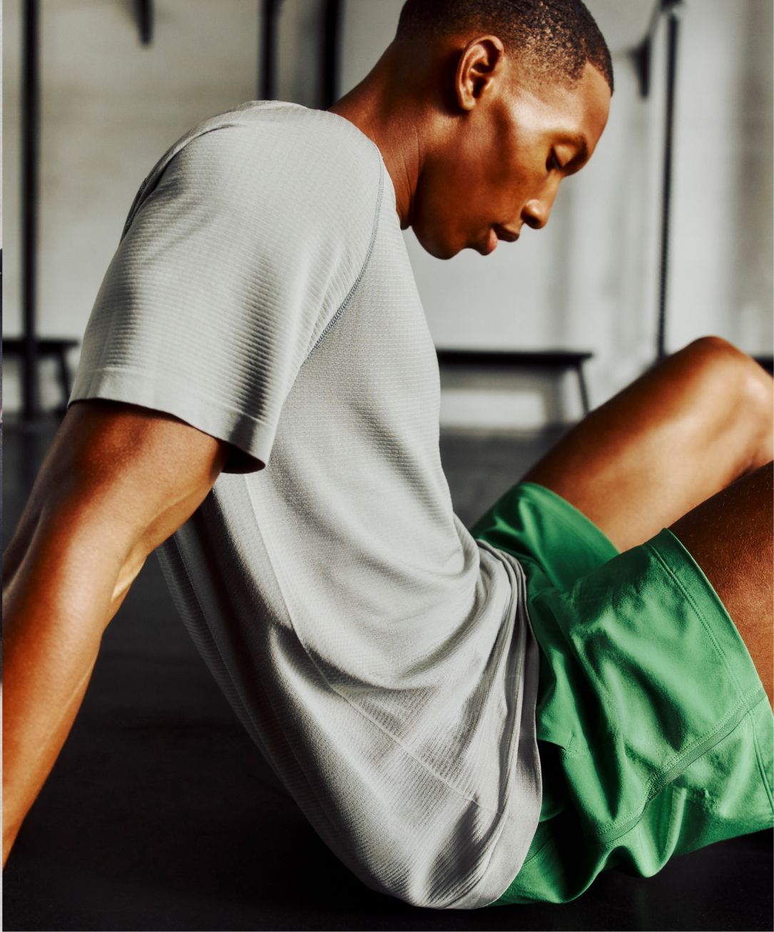 A person sits, leaning back, to take a breather while working out in a gym. They wear the Metal Vent Tech Shirt.