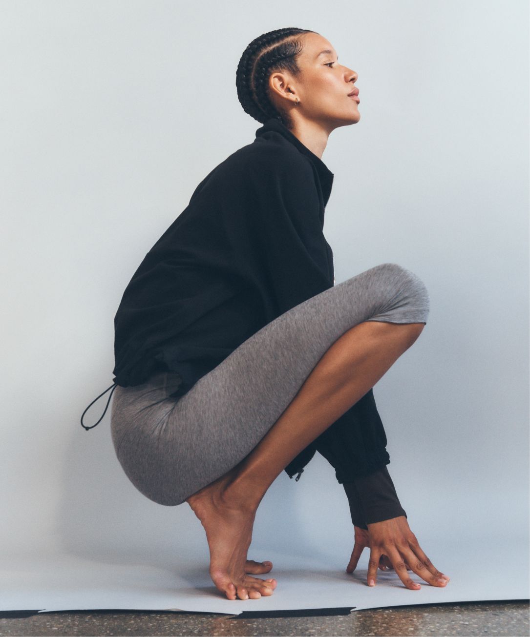A person crouching on a neutral backdrop. They're wearing the lululemon Ultralight WovenAir Jacket and Align High-Rise Crop.