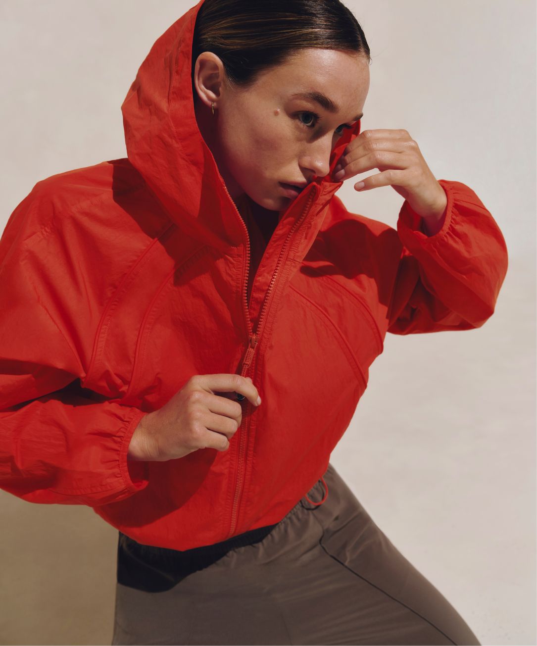 A person poses while holding the collar of their Scuba Windbreaker. They are also wearing the Breezily Pants in Nomad and the Scuba Windbreaker in Cherry Ember.
