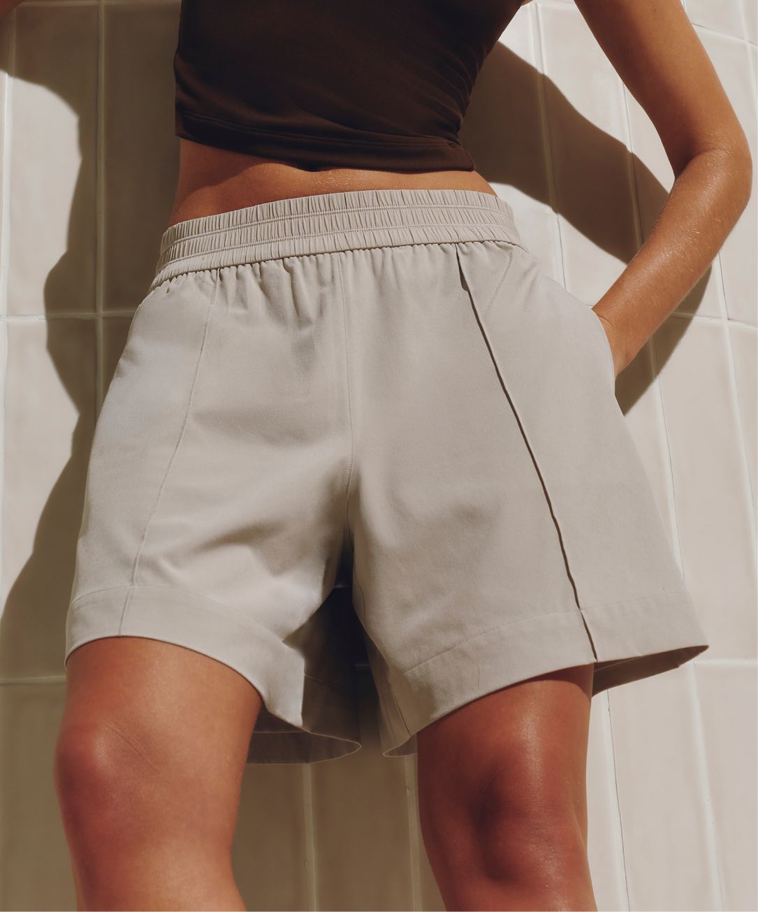 A person poses in front of a tiled wall. They are wearing the Breezily Shorts in Downtown Tan and Align Mini V-Neck Tank in Walnut Crunch.