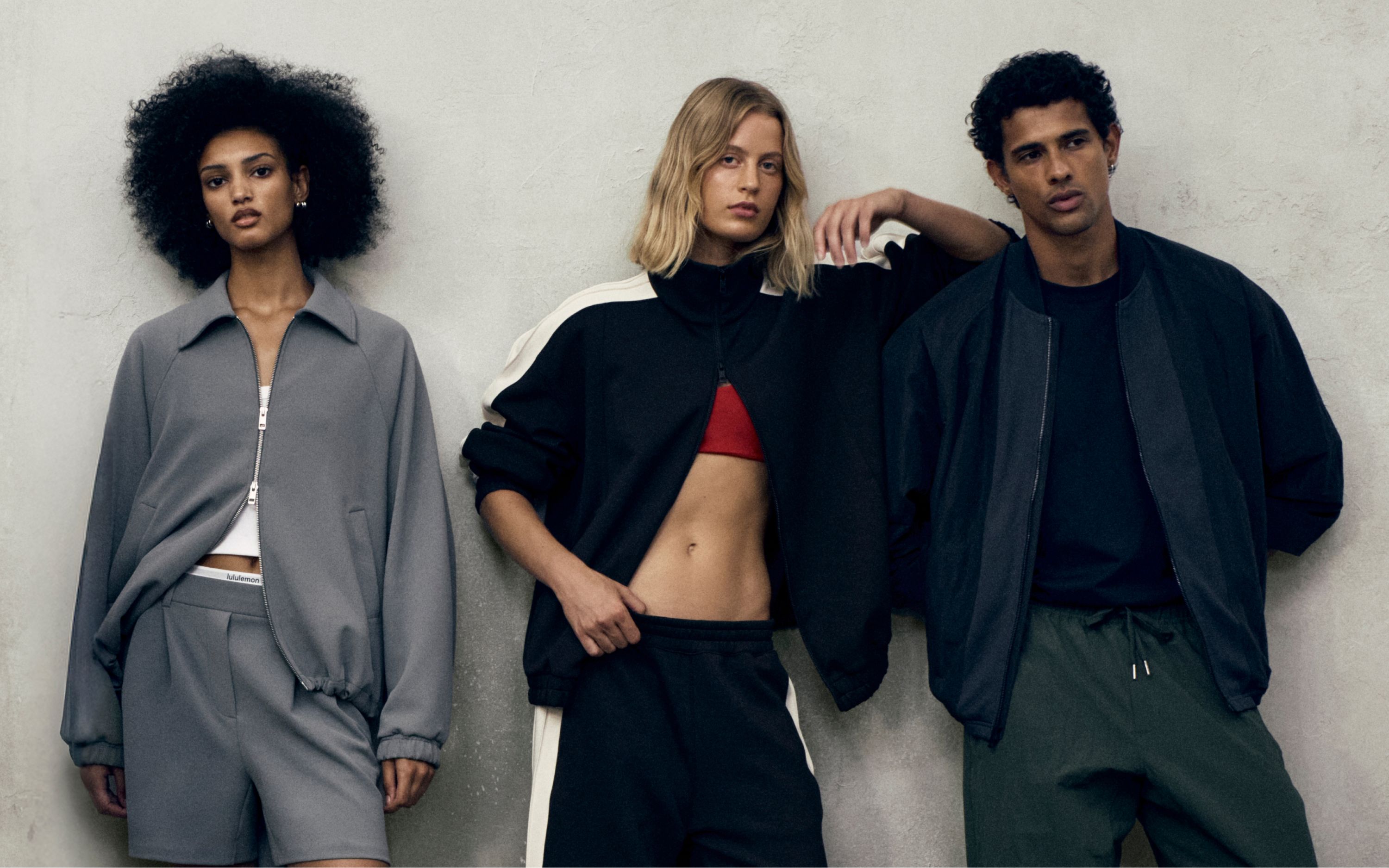 Three people pose leaning against a grey wall. The person in the middle has their arm on another person's shoulder. All three people are wearing new styles from the fall 2026 line.