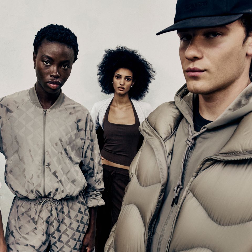 Three people pose leaning against a grey wall. They are wearing new styles from the fall 2026 line.  