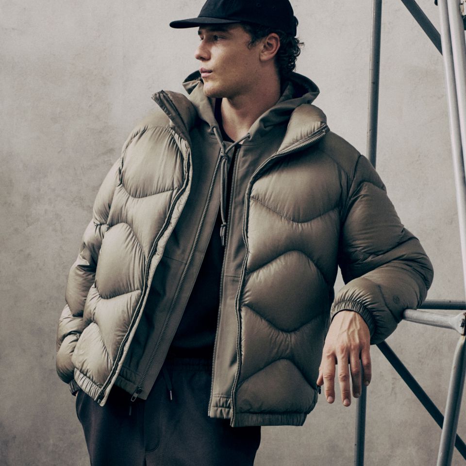 A person looks to the side leaning against a metal structure. They are wearing new styles from the fall 2026 line.