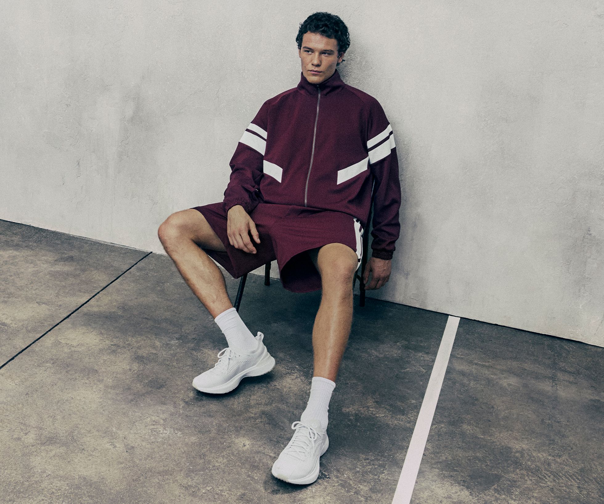 A person sitting on a chair leaning back against a wall, wearing a lululemon Track jacket and matchign shorts. 