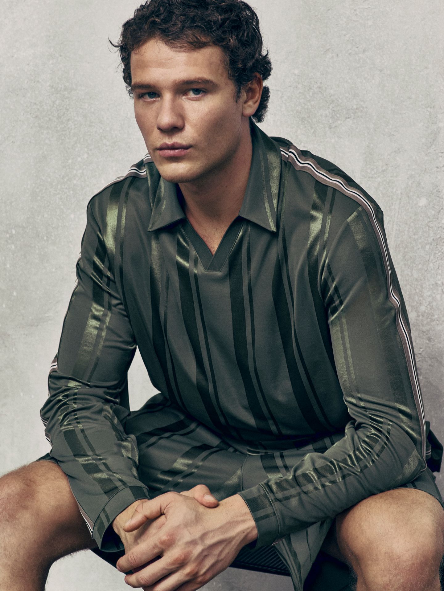 A person sits on a bench, leaning forward with their arms resting on their thighs. They are wearing new styles from the fall 2026 line.