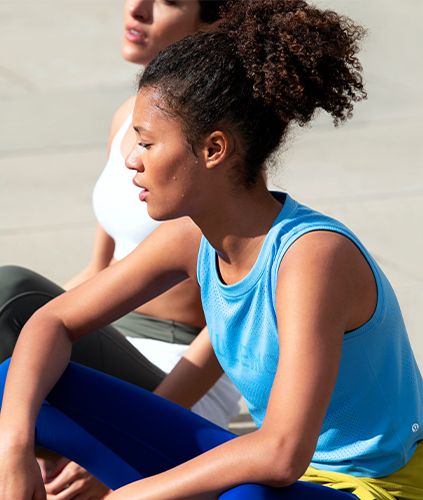 One woman wearing the Breeze By Muscle Tank sitting next to another woman.